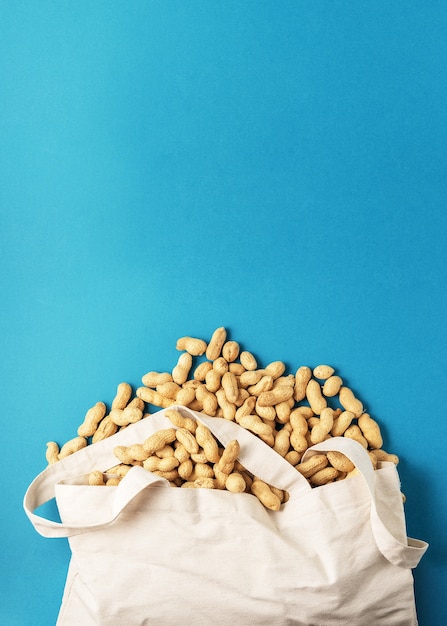 Getrocknete rohe Erdnüsse von einer Stofftasche auf einem blauen Hintergrund