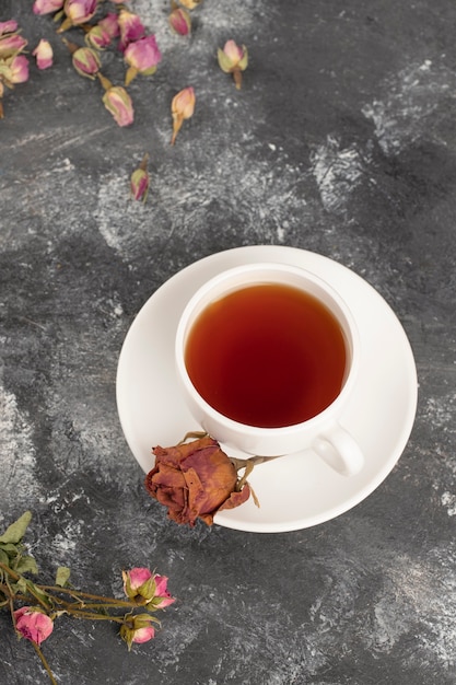 Getrocknete Rosenknospen mit einer Tasse heißen Tees auf einem Steintisch.