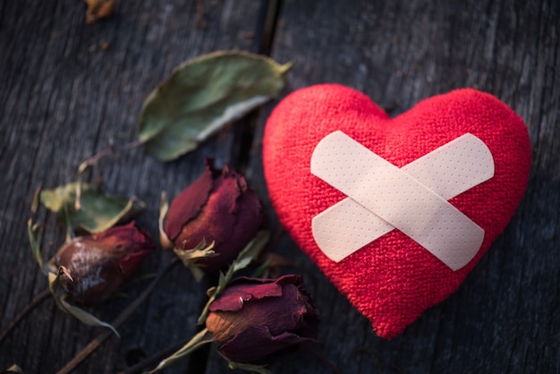 Getrocknete Rotrose mit rotem Papier in Form des defekten Herzens auf hölzernem Hintergrund