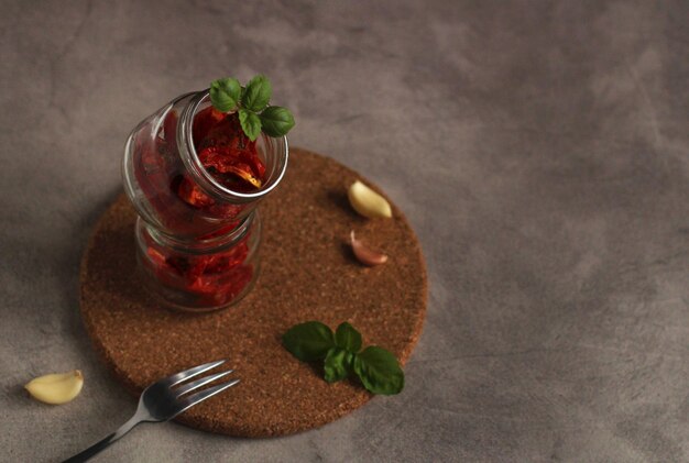 Getrocknete Tomaten in einem Glas mit Knoblauch und Basilikum auf grauem Hintergrund