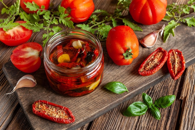 Getrocknete Tomaten in einem Glasgefäß mit Olivenöl mit Knoblauch und Gewürzen. Einmachen zu Hause, Dehydration. Nahaufnahme, selektiver Fokus auf Vintage-Holz-Hintergrund