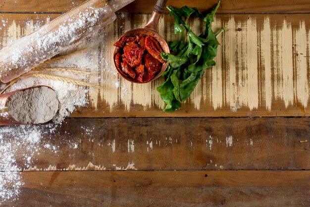 Getrocknete Tomaten in kleinem Kupfertopf, Nudelholz, Rucola und Mehl auf dem Holztisch mit freiem Platz für Text, Draufsicht, Kopienraum.