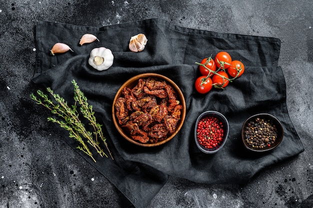 Getrocknete Tomaten mit Knoblauch, Gewürzen und Kräutern. Rezept zum Kochen mit Zutaten. Schwarzer, dunkler Hintergrund.