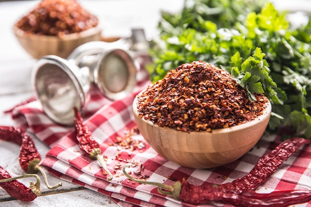 Getrocknete und zerkleinerte Chilischoten in Holzschalen mit Petersilienkräutern.