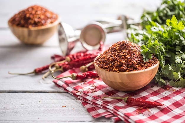 Getrocknete und zerkleinerte Chilischoten in Holzschalen mit Petersilienkräutern.