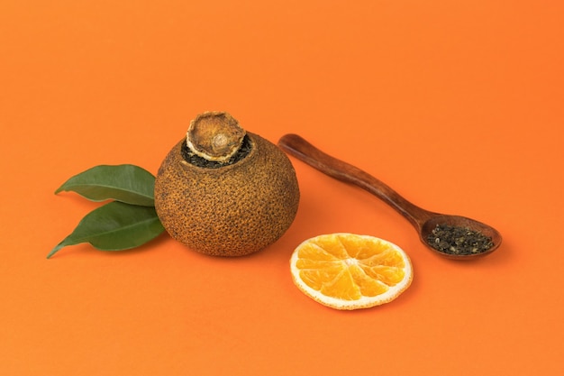 Getrockneter Orangentee und ein Holzlöffel auf einem orangefarbenen Hintergrund.