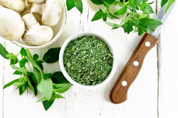 Getrockneter Oregano in Schüssel Oregano verzweigt sich mit Blättern in Mörserchampignons und einem Messer auf Holzbretthintergrund von oben