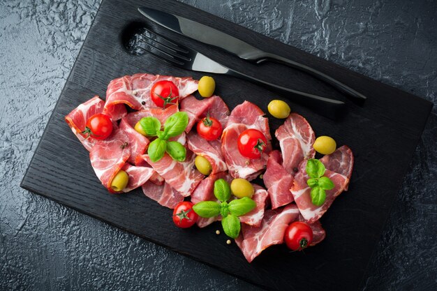 Getrocknetes Fleisch, Jamon mit Kirschtomaten, Basilikum und Oliven auf einem schwarzen