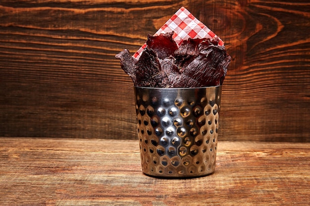 Getrocknetes gepfeffertes Beef Jerky in Streifen geschnitten in einem Metalleimer auf Holzhintergrund Servieren des Gerichts in einem Restaurant