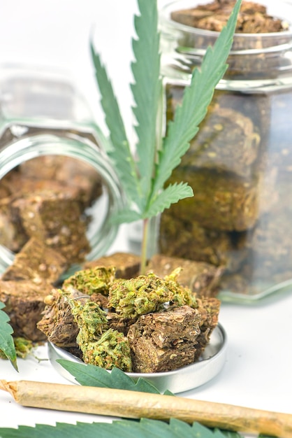 Getrocknetes Marihuana in einem Glas mit grünen Marihuana-Blättern und Rollen auf weißem Hintergrund Medizinische Marihuana-Apotheke Alternative Medizin Cannabis-Plantage für Medizin- und Geschäftskonzept