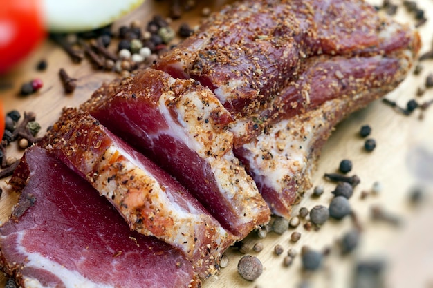 Getrocknetes und gewürztes Fleisch auf einem Holzbrett geschnitten, Gewürze, Pfeffer, Zitrone, grüner Rosmarin und das Fleisch ist fertig zum Essen