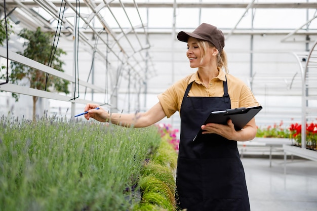 Gewächshausarbeiterin mit Klemmbrett inspiziert Blumen