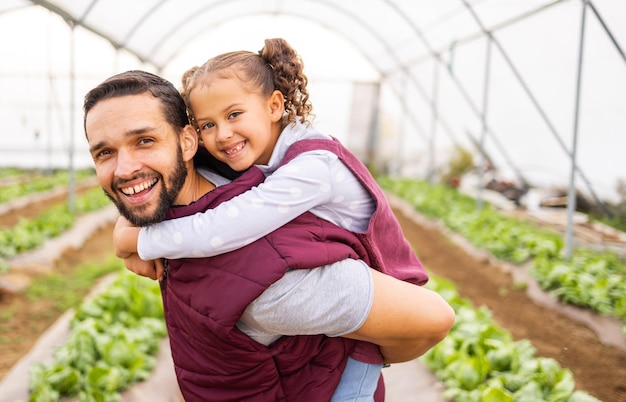 Gewächshausbauer Vater mit Mädchen und glückliches Lächeln des Mädchens, das Huckepack vom Vater in einem Bio-Bauernhof für nachhaltiges Pflanzenwachstum bekommt Gesunde Lebensmittel produzieren natürliche Pflanzen und moderne Landwirtschaft