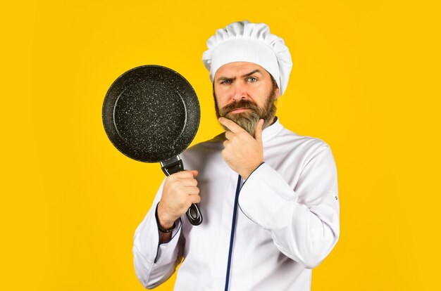 Gewerbliche Küche kocht leckeres Gericht. Bärtiger Mann hält Bratpfanne in der Hand. Kochen im Topf zur Zubereitung von Speisen. Bärtiger Mann kocht in der Küche, kulinarisch und in der Küche. Küchenutensilien. Gesundes Essen kochen