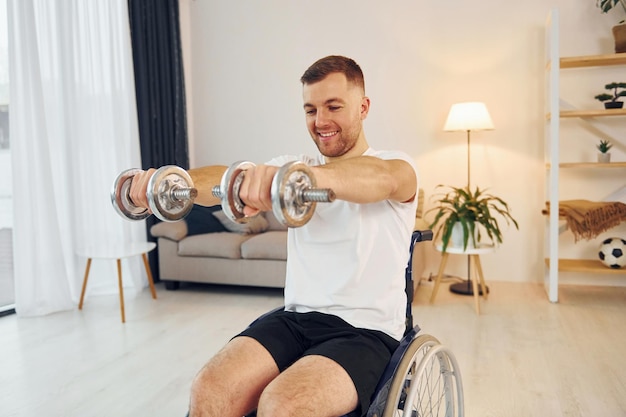 Gewichte halten Behinderter Mann im Rollstuhl ist zu Hause