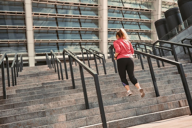 Foto gewichtsverlust rückansicht einer jungen frau in übergröße in sportkleidung, die auf treppen joggt