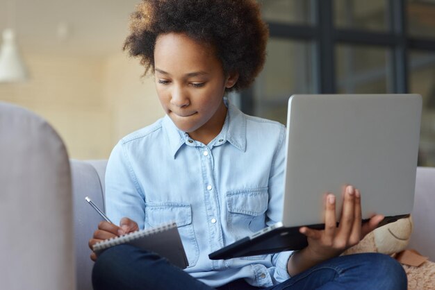 Gewinnen Sie neues Wissen, das sich auf ein jugendliches Schulmädchen konzentriert, das einen Laptop hält und während des Online-Unterrichts Notizen macht