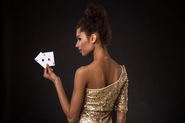 Gewinnende Frau - Junge Frau in einem noblen Goldkleid, das zwei Asse hält, eine Kartenkombination des Pokers der Asse.
