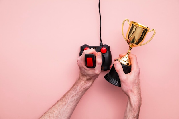 Gewinnende Gamer-Hand mit einem Retro-Games-Joystick mit einer goldenen Trophäe