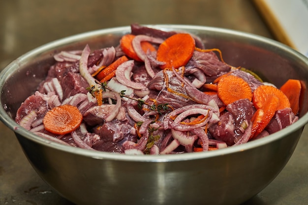 Gewürfeltes Rindfleisch mit Zwiebeln und Karotten in Metallschüssel zum Kochen bereit