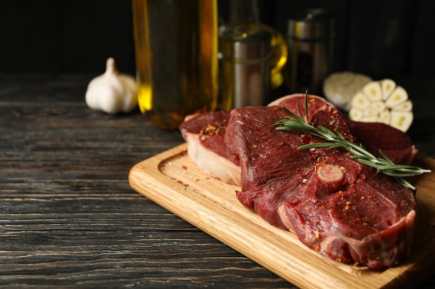 Gewürze, Öl und Brett mit rohem Steakfleisch auf Holztisch