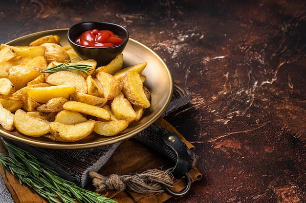 Gewürzte Kartoffelspalten mit Rosmarin und Tomatensauce in einem Teller Dunkler Hintergrund Draufsicht Kopierbereich