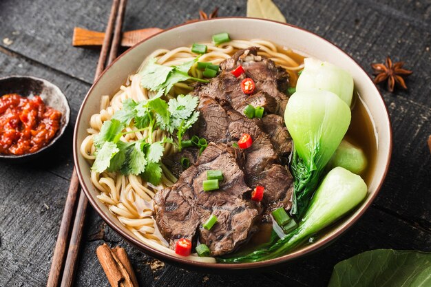 Gewürzte rote Suppe mit Rindfleisch-Nudeln in einer Schüssel auf einem Holztisch
