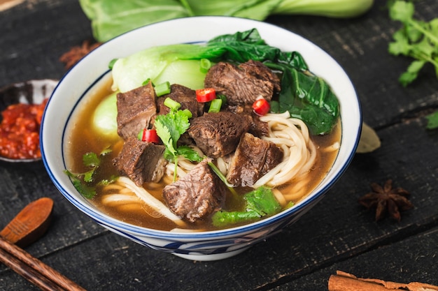 Gewürzte rote Suppe mit Rindfleisch-Nudeln in einer Schüssel auf einem Holztisch