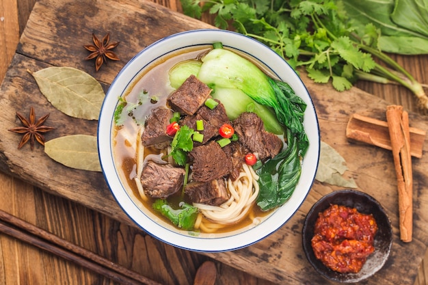 Gewürzte rote Suppe mit Rindfleisch-Nudeln in einer Schüssel auf einem Holztisch