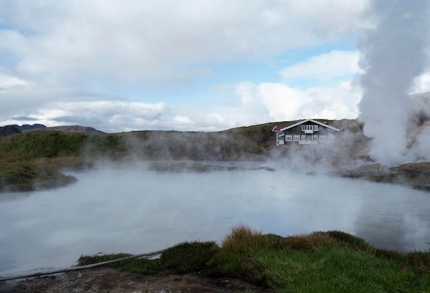 Geysir in einer isländischen Landschaft neben einem Haus