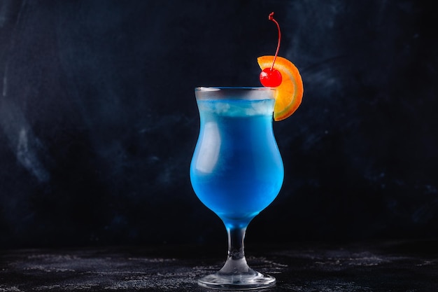gGass de cóctel laguna azul decorado con naranja y cereza en el fondo del mostrador del bar festivo