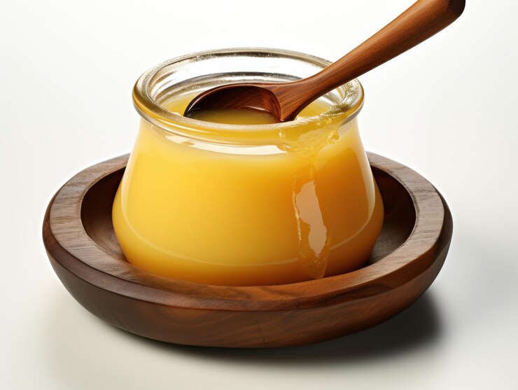 Ghee dorado en un frasco de vidrio con cuchara de madera en un plato