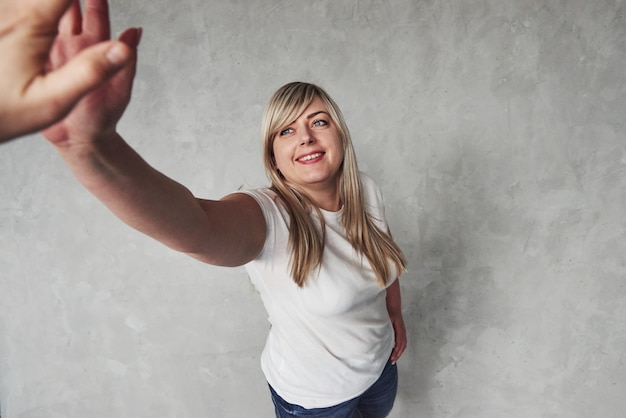 Foto gib mir deine high five. junge weiße frau, die gegen grauen raum steht