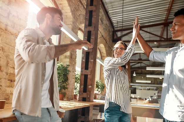 Gib mir fünf junge Männer und Frauen, die High-Five geben, während sie eine Kaffeepause mit Kollegen in der