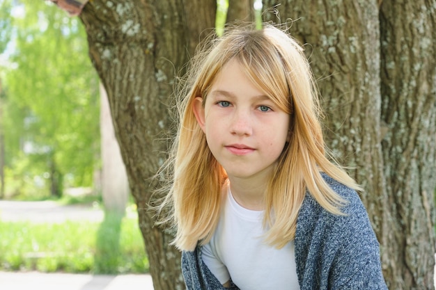 Giel adolescente con cabello rubio cerca de la naturaleza de verano del árbol