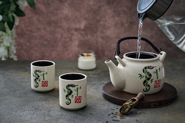 Gießen Sie aus dem Wasserkocher kochendes Wasser in die Teekanne für die Teezeremonie mit einem alten Keramikservice