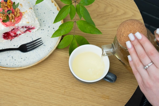 Gießen Sie Buchweizentee in eine Tasse und legen Sie eine Baiserrolle auf den Tisch im Café. Stillleben mit süßen Speisen