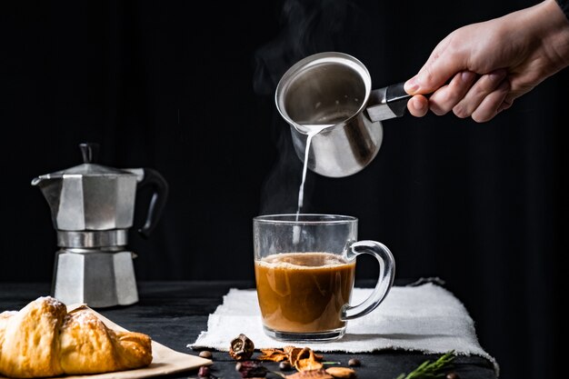 Gießen Sie dampfende Milch in eine Tasse Kaffee. Hinzufügen von heißer Milch zu Espressokaffee, der in italienischem Moka gebraut wird, zurückhaltender Schuss