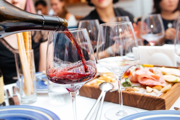 Gießen Sie Rotwein in ein Glas im Restaurant mit Vorspeisen