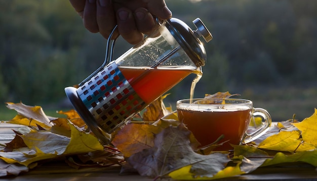 Gießen Sie Tee in eine Tasse auf dem Hintergrund des Sonnenuntergangs mit herbstgelben Blättern