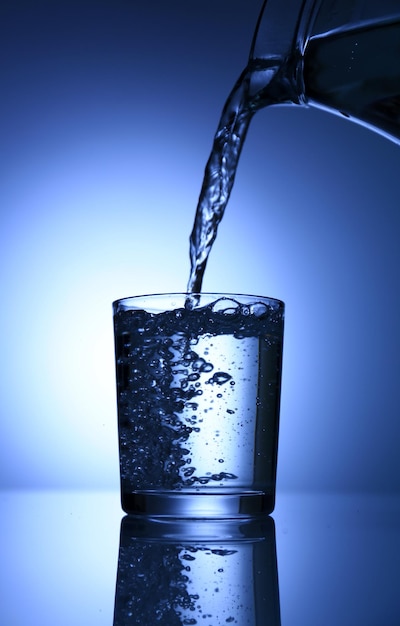 Gießen Sie Wasser aus dem Krug in Glas auf dunkelblauem Hintergrund