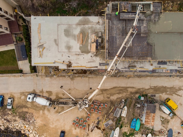 Gießen von Betonzement auf das Dach eines im Bau befindlichen Wohngebäudes mit einer Betonpumpen-LKW-Maschine mit hohem Ausleger, um die Mischung in die oberen Stockwerke zu liefern Luftbild