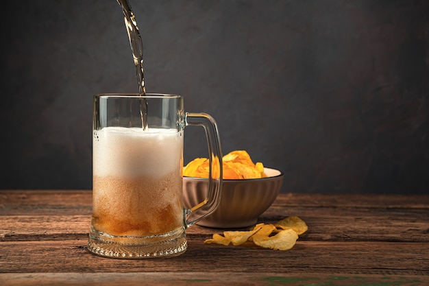 Gießen von Bier in ein Bierglas auf dem Hintergrund von Kartoffelchips. Seitenansicht, Platz zum Kopieren.