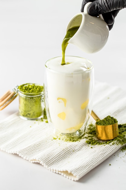 Gießen von grünem Matcha-Tee in Eisglas mit Milch