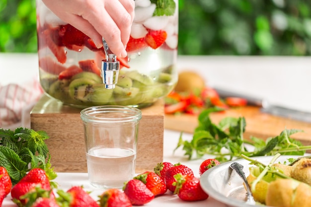Gießen von infundiertem Wasser mit Bio-Erdbeeren, Kiwi und frischer Minze aus einem Getränkespender aus Glas.