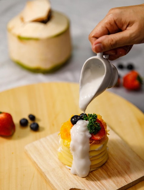 Gießen von Kokosmilchsauce auf köstlichen Crêpe-Kuchen, dekoriert mit goldenen Eigelbfäden, Foi Thong Crêpe-Kuchen auf einem Holzteller