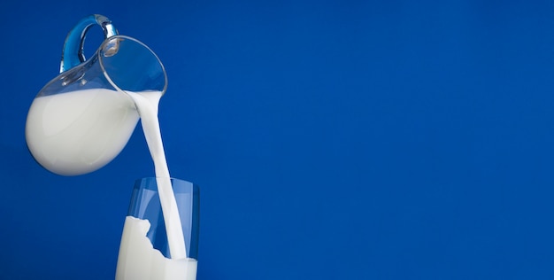 Gießen von Milch mit Spritzer auf blauem Hintergrund