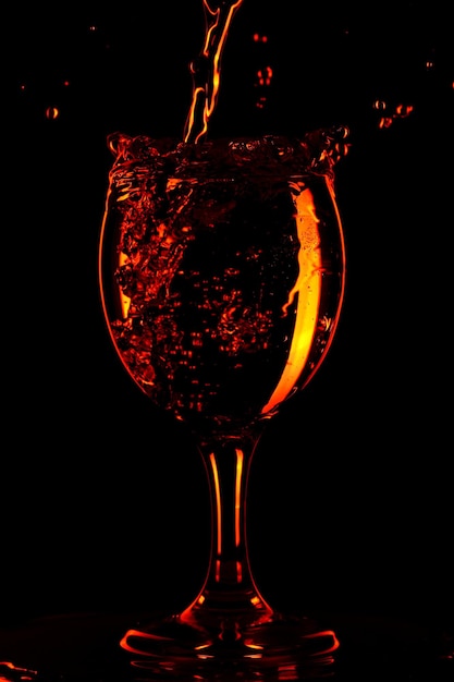 Gießen von Wasser in ein Glas auf schwarzem Hintergrund. Orangenwasser in einem Glas