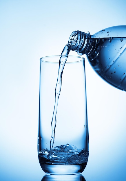 Gießen von Wasser in Glas aus Flasche auf blauem Hintergrund