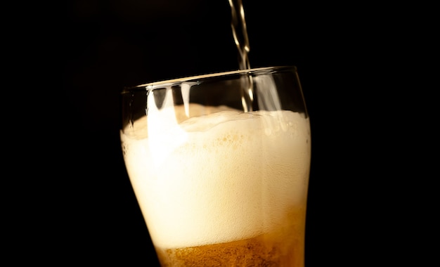 gießt Bier in ein Glas auf einem dunklen Hintergrund